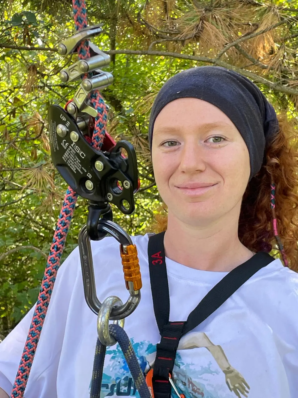 Portrait de Chloé Dufetel souriante, bandeau sur les cheveux, corde, poulie et mousquetons de grimpe à côté d’elle